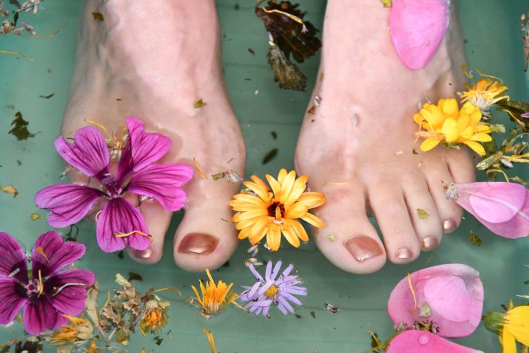 nackte Füße in hellgrüner Wanne mit Wasser und lila-, rosafarbenen und gelben Blumen