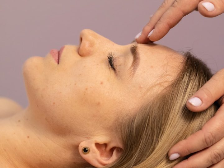 Frau erhält eine entspannende Kopf- und Gesichtsmassage mit geschlossenen Augen.