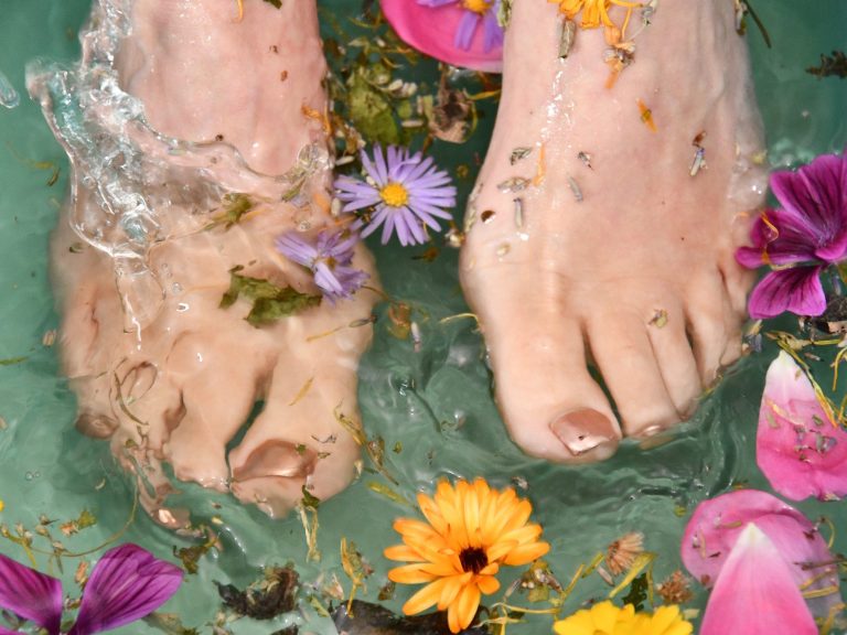 Zwei nackte Füße plantschen in einer hellgrünen Wanne mit Wasser und bunten Blumen herum.